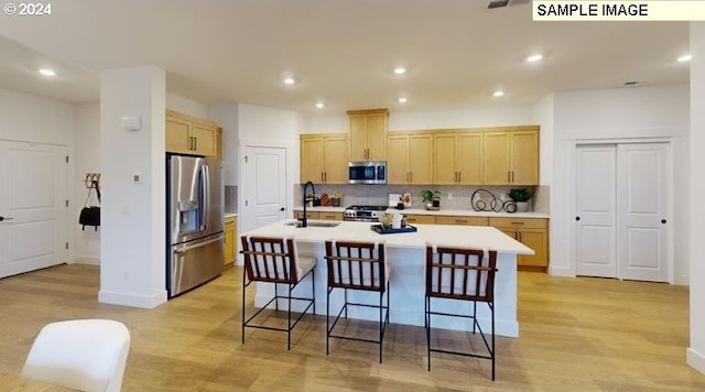 kitchen featuring sink, light hardwood / wood-style flooring, stainless steel appliances, backsplash, and a center island with sink