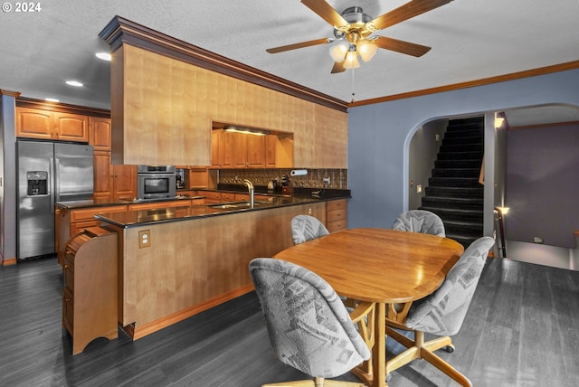 kitchen with kitchen peninsula, appliances with stainless steel finishes, dark wood-type flooring, and ornamental molding