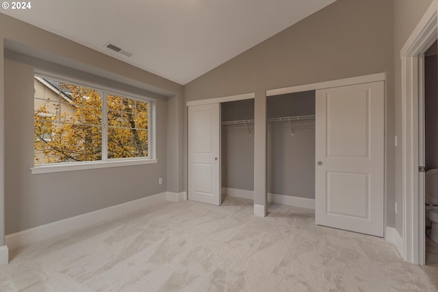 unfurnished bedroom featuring light colored carpet, multiple closets, and lofted ceiling