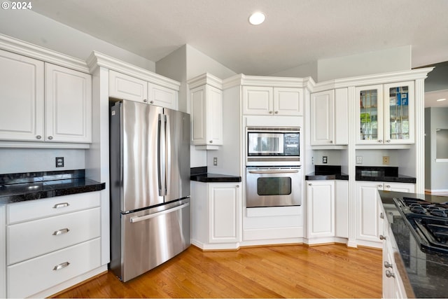 kitchen featuring white cabinetry, appliances with stainless steel finishes, vaulted ceiling, and light wood-type flooring