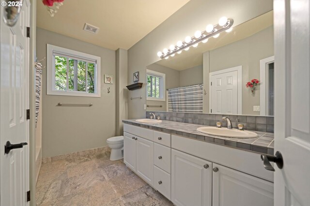 bathroom with decorative backsplash, toilet, dual bowl vanity, and tile patterned flooring