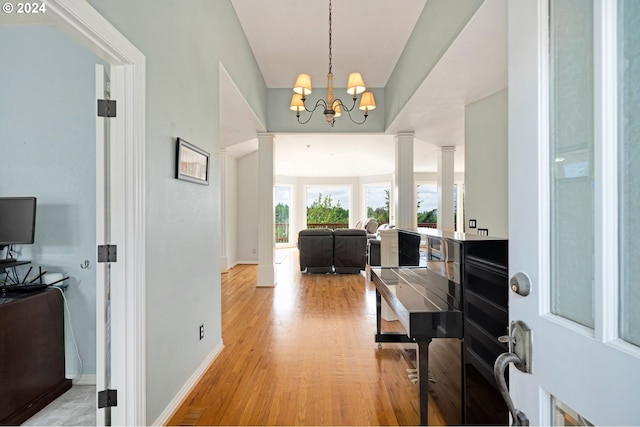 hall with light wood-type flooring, decorative columns, and an inviting chandelier