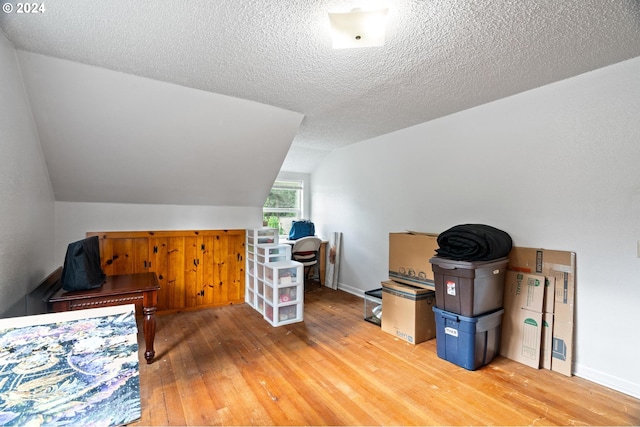 interior space with light hardwood / wood-style flooring, a textured ceiling, and vaulted ceiling