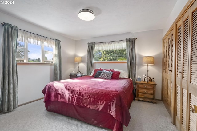 bedroom featuring a textured ceiling, light carpet, multiple windows, and a closet