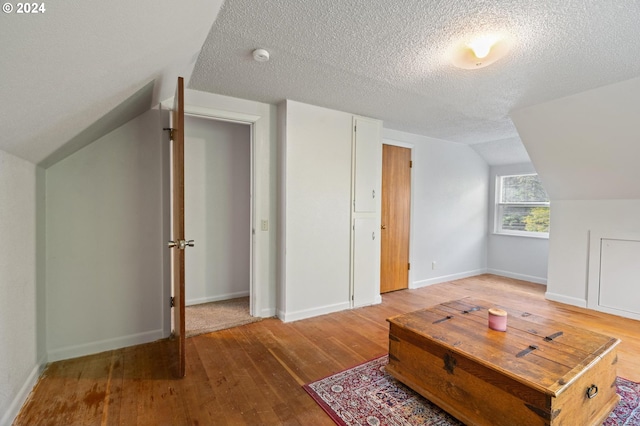 bonus room with lofted ceiling, hardwood / wood-style floors, and a textured ceiling