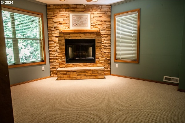 unfurnished living room featuring carpet flooring, a stone fireplace, ceiling fan, and ornamental molding