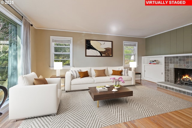 living area with a tiled fireplace, wood finished floors, a wealth of natural light, and ornamental molding