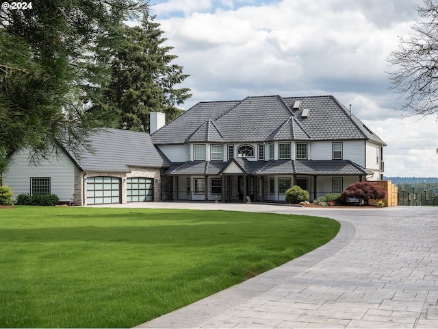 view of front facade with decorative driveway, a tile roof, a chimney, a garage, and a front lawn