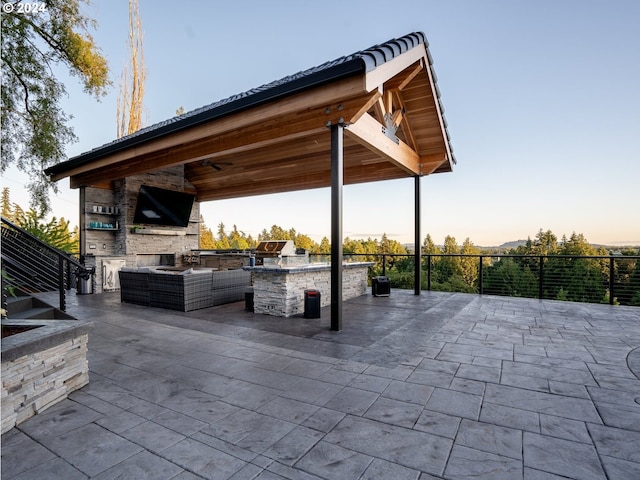 view of patio with a gazebo, an outdoor kitchen, ceiling fan, and an outdoor stone fireplace