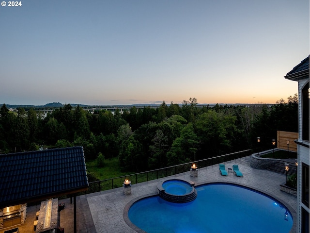 view of swimming pool featuring a pool with connected hot tub, a patio area, and a view of trees