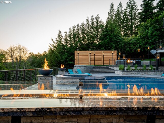 pool at dusk with an in ground hot tub and a patio area