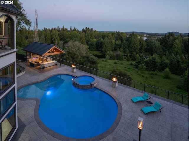 pool at dusk featuring a gazebo, an outdoor fire pit, an in ground hot tub, and a patio area