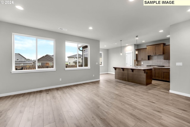 kitchen with light hardwood / wood-style floors, a center island with sink, hanging light fixtures, and a breakfast bar area