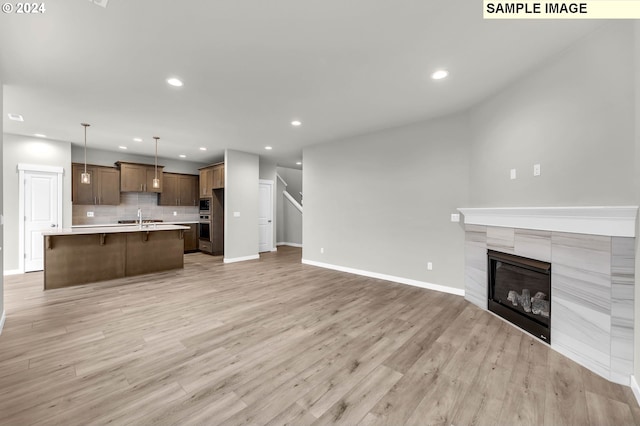 unfurnished living room with a tile fireplace, sink, and light hardwood / wood-style floors