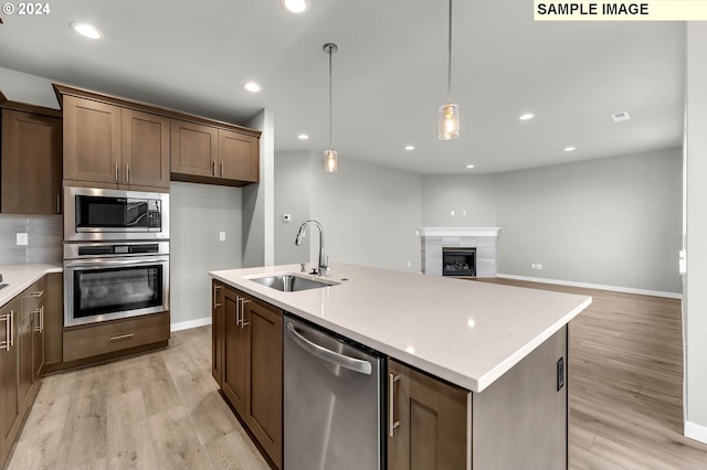 kitchen with appliances with stainless steel finishes, light wood-type flooring, a kitchen island with sink, sink, and pendant lighting