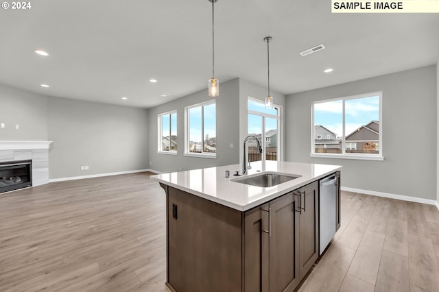 kitchen with a tile fireplace, sink, hanging light fixtures, stainless steel dishwasher, and light hardwood / wood-style floors