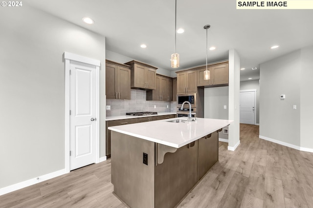 kitchen featuring an island with sink, appliances with stainless steel finishes, pendant lighting, and light wood-type flooring