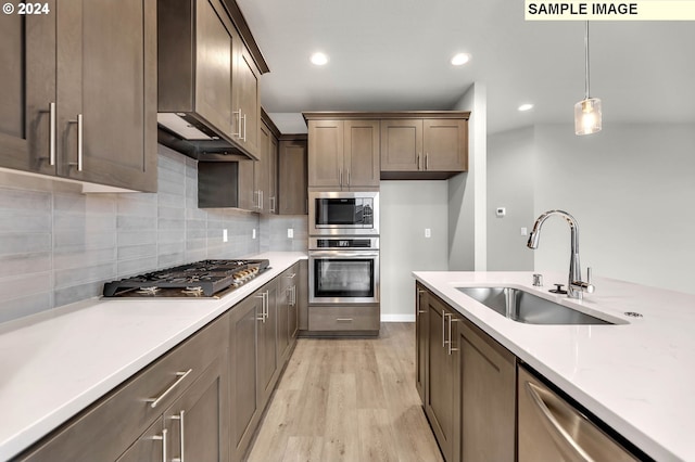 kitchen featuring light stone countertops, appliances with stainless steel finishes, wall chimney exhaust hood, decorative light fixtures, and light hardwood / wood-style floors