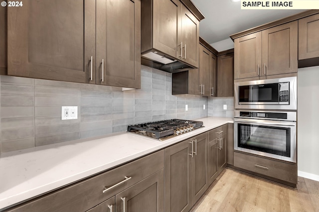 kitchen with custom exhaust hood, tasteful backsplash, stainless steel appliances, and light hardwood / wood-style flooring