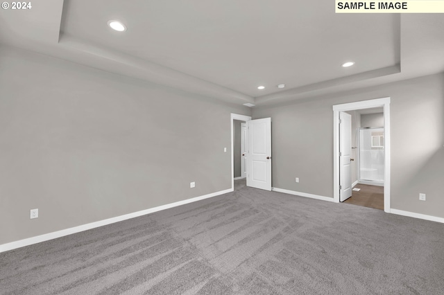 unfurnished bedroom featuring a tray ceiling, connected bathroom, and dark colored carpet