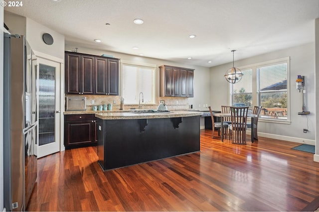 kitchen featuring tasteful backsplash, a center island, dark hardwood / wood-style flooring, decorative light fixtures, and light stone counters