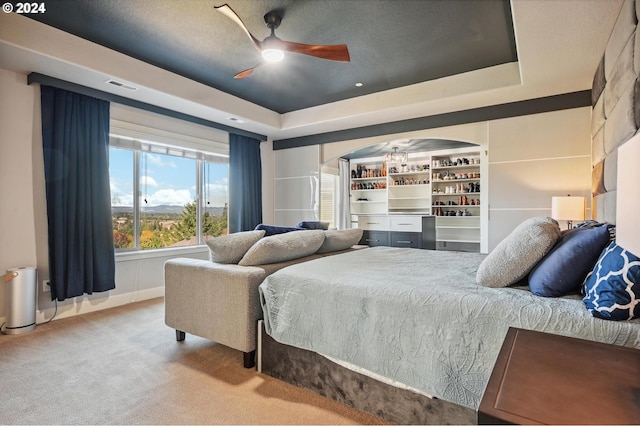 bedroom featuring ceiling fan, light carpet, a textured ceiling, and a tray ceiling