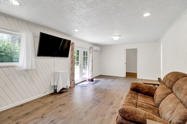 living room featuring a textured ceiling, wood finished floors, baseboards, french doors, and an AC wall unit