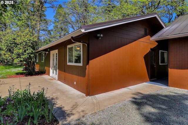 view of side of home with french doors, a patio area, a standing seam roof, and metal roof