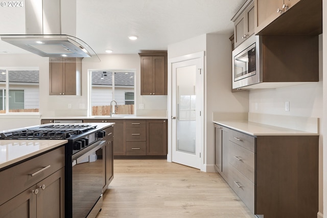 kitchen with island range hood, sink, stainless steel appliances, and light hardwood / wood-style flooring