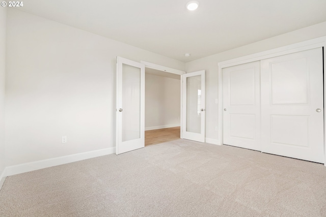 unfurnished bedroom with a closet, light carpet, and french doors