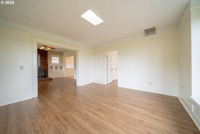 spare room with light hardwood / wood-style floors, a wood stove, ceiling fan, and ornamental molding