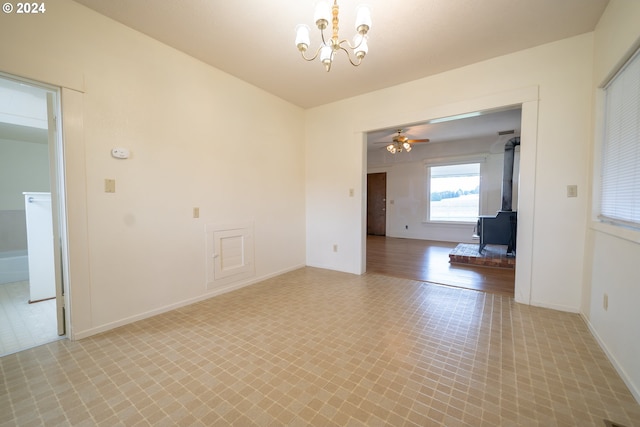 empty room featuring ceiling fan with notable chandelier and a wood stove