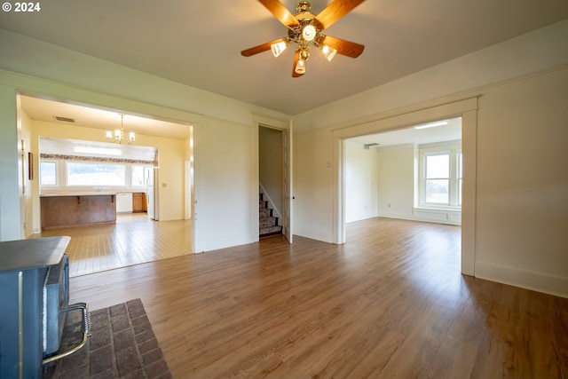 unfurnished living room featuring hardwood / wood-style floors, ceiling fan with notable chandelier, and plenty of natural light