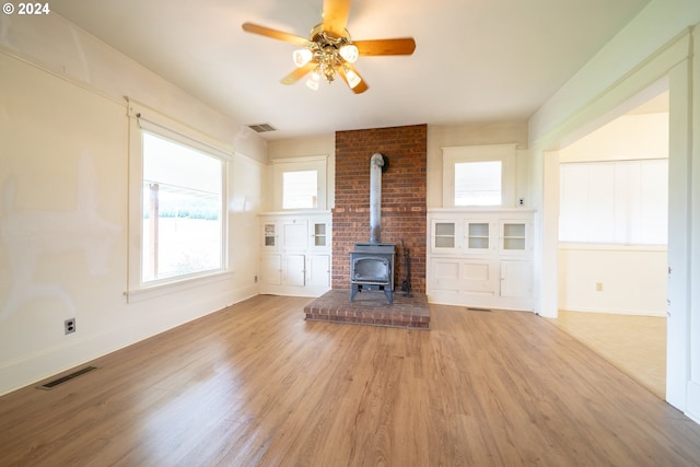 unfurnished living room featuring a wood stove, ceiling fan, and light wood-type flooring