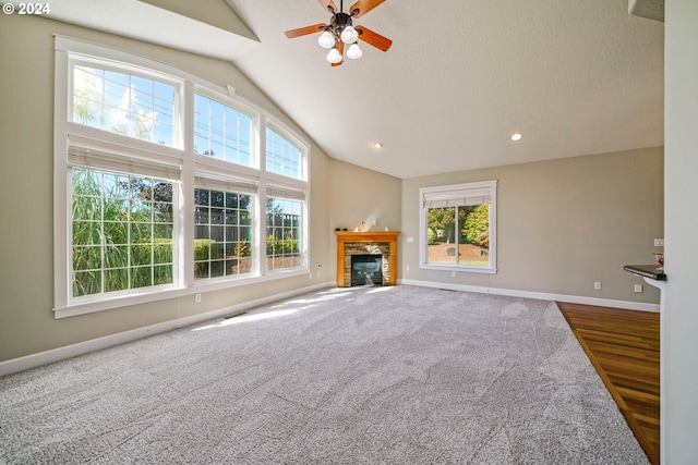 unfurnished living room featuring a wealth of natural light, vaulted ceiling, ceiling fan, and a stone fireplace