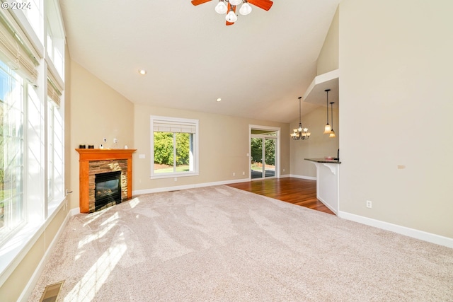 unfurnished living room with ceiling fan with notable chandelier, a stone fireplace, wood-type flooring, and high vaulted ceiling