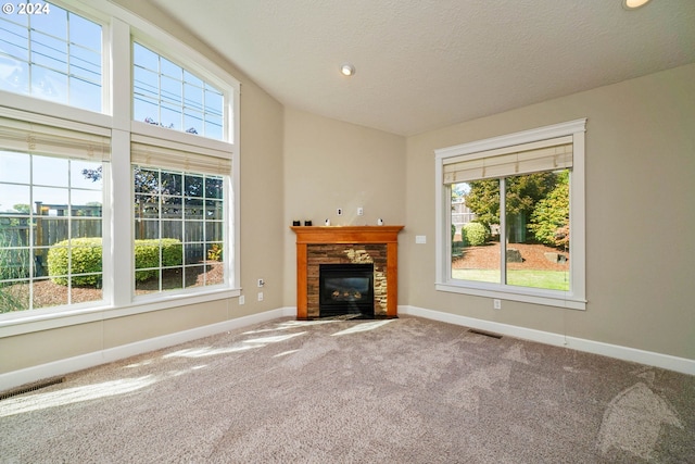 unfurnished living room with a stone fireplace, a textured ceiling, and carpet flooring