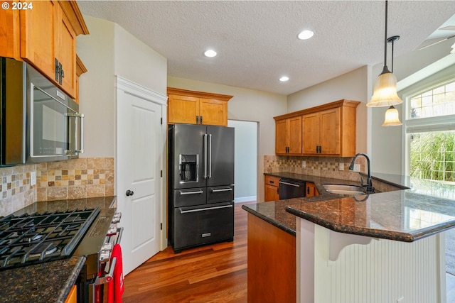 kitchen with sink, high end appliances, kitchen peninsula, hanging light fixtures, and decorative backsplash