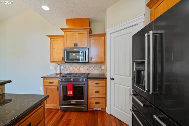 kitchen with a textured ceiling, dark wood-type flooring, backsplash, dark stone countertops, and high quality appliances