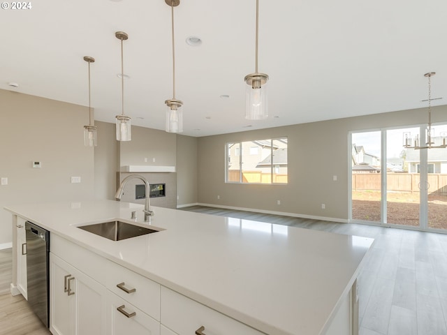 kitchen featuring light hardwood / wood-style floors, a kitchen island with sink, pendant lighting, sink, and white cabinets