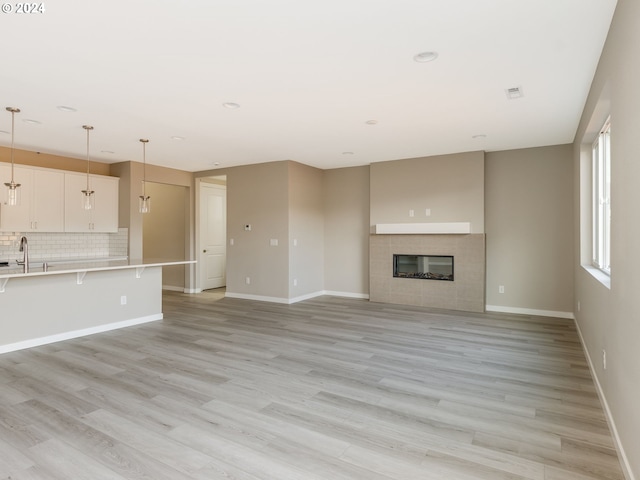 unfurnished living room with light hardwood / wood-style flooring, sink, and a tile fireplace