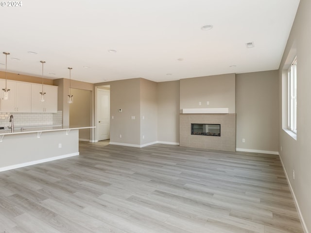 unfurnished living room with a fireplace, sink, and light hardwood / wood-style floors