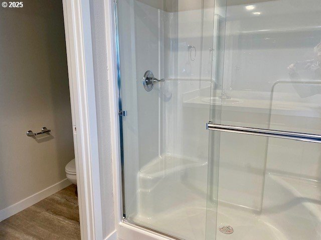 bathroom with a stall shower, baseboards, toilet, and wood finished floors