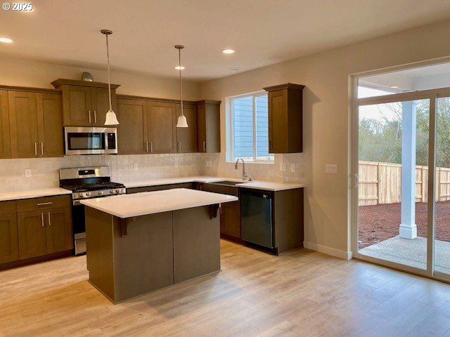 kitchen featuring sink, tasteful backsplash, hanging light fixtures, appliances with stainless steel finishes, and light hardwood / wood-style floors