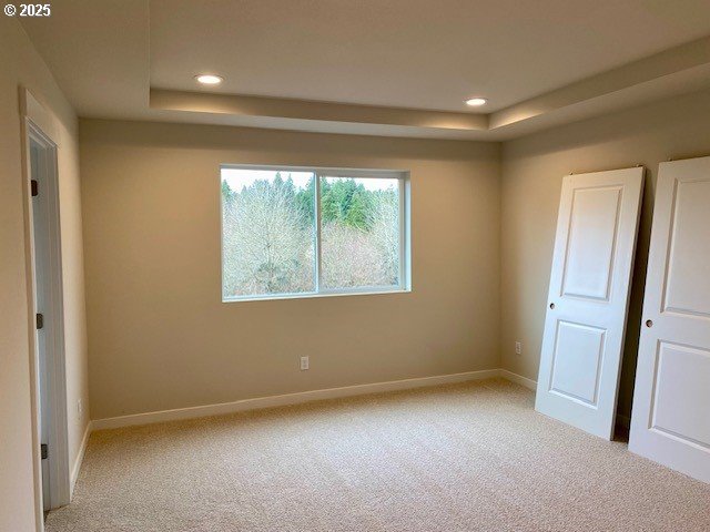 unfurnished bedroom featuring light carpet, baseboards, a tray ceiling, and recessed lighting