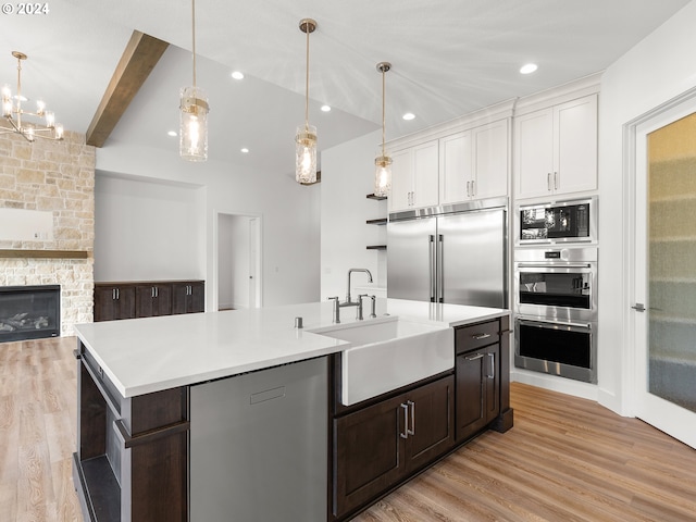 kitchen with built in appliances, white cabinetry, a center island with sink, and a stone fireplace