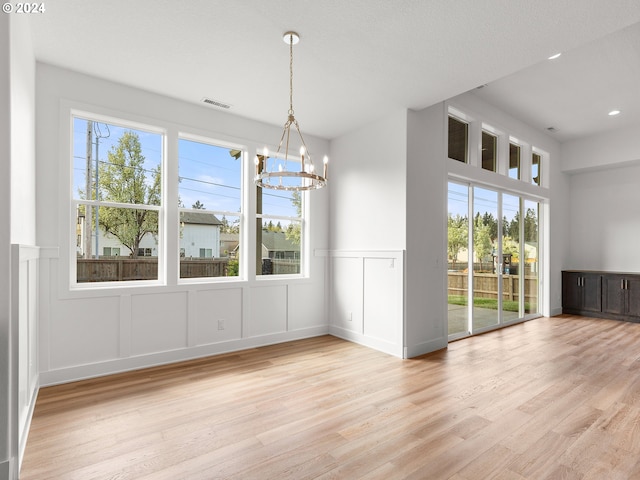 unfurnished dining area with a chandelier, a healthy amount of sunlight, a textured ceiling, and light hardwood / wood-style flooring