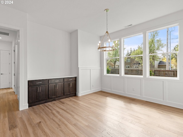 unfurnished dining area featuring an inviting chandelier and light wood-type flooring