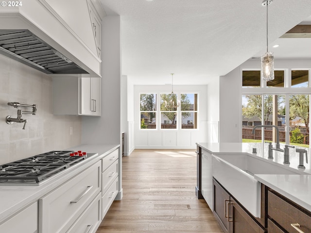 kitchen with white cabinets, light hardwood / wood-style floors, hanging light fixtures, and custom exhaust hood