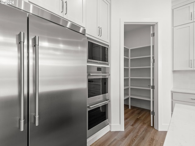 kitchen with built in appliances, light stone countertops, light wood-type flooring, and white cabinetry